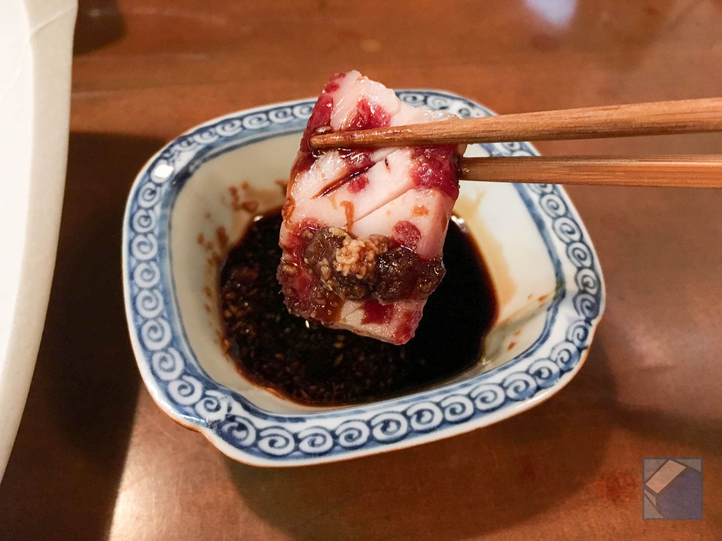 Close-up of horse sashimi being dipped in soy sauce with ginger and garlic